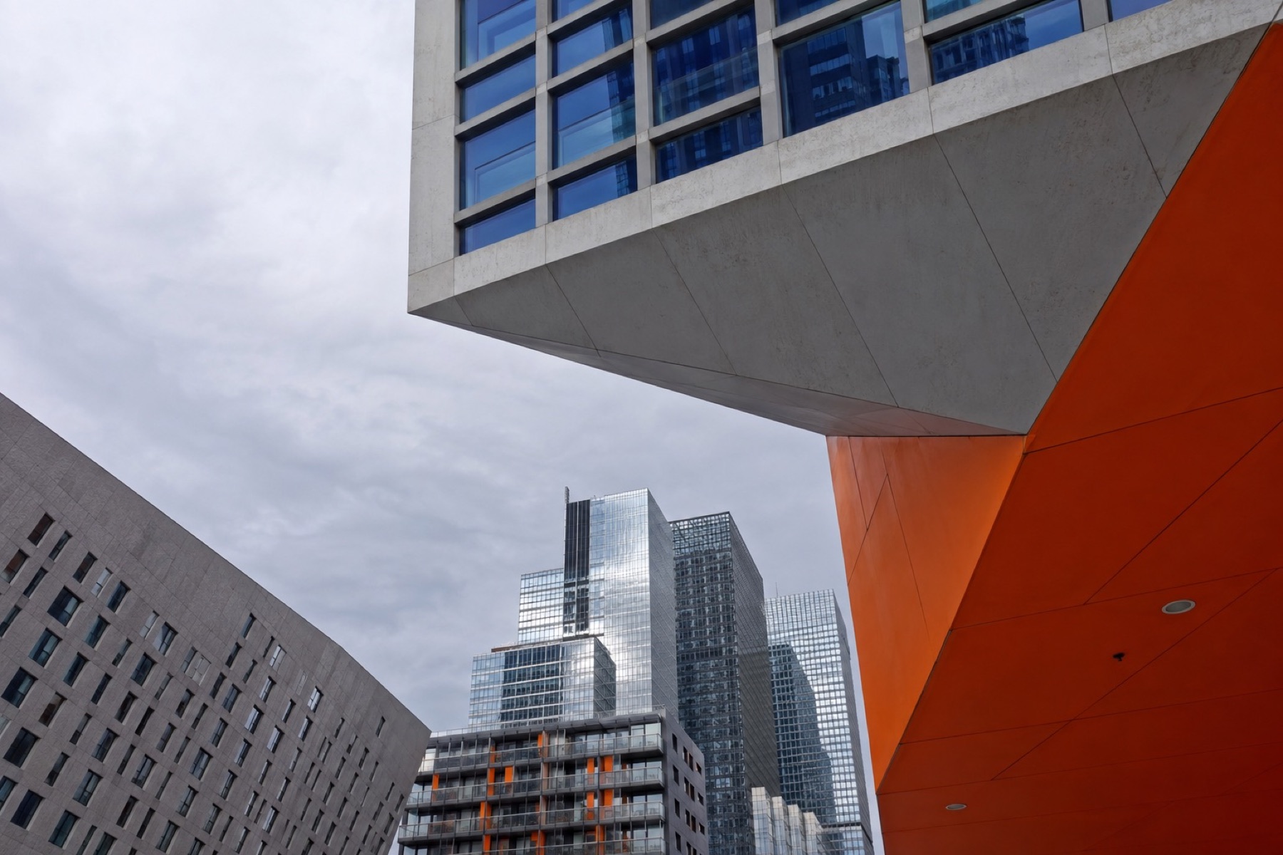 Hoogbouw van onderaf gezien, een oranje gevelvlak tegen de wolken